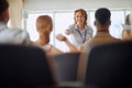 Female lecturer communicating with students, pointing at one of them with a smile