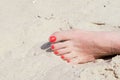Female left foot on the sand, on the beach. Nails painted with red varnish