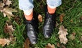 Female legs in black boots on green grass with yellow fallen autumn leaves in the park. Autumn concept. Womens shoes in autumn Royalty Free Stock Photo