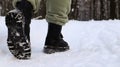 Female legs in black boots, winter walk in the snow. Active woman walking away from the camera in the winter forest. Focus on your