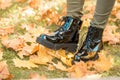 Female legs in black patent leather boots standing on a carpet of yellow fallen maple leaves while walking in an autumn park. Royalty Free Stock Photo