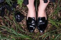Female legs in black patent leather shoes on the grass