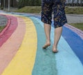 Female legs close up on barefoot on wet asphalt drawn rainbow walking path after rain among puddles, copy space, love, freedom and Royalty Free Stock Photo