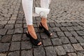 Female legs in elegant black summer shoes in trendy white jeans with a leather bag on the street. Close-up Royalty Free Stock Photo