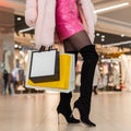 Female legs in fashionable black shoes with colorful paper shopping bags in store. Chic young woman in luxury clothes walks on