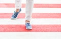 Female legs or feet crossing red crosswalk at summer day. Woman dressed in white jeans and blue loafers walking through