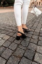 Female legs in jeans in black leather sandals with a bag on a stone road in the city. Close-up Royalty Free Stock Photo