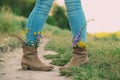 Female legs in jeans high boots with inserted flowers on the road in the field Royalty Free Stock Photo