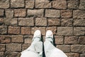 Female legs in jeans and white sneakers on paving stones. Teenage feet top view. Prague street, old city Royalty Free Stock Photo