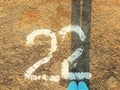 Female legs in sneakers stand on the asphalt road and number 22 Royalty Free Stock Photo