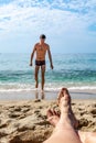 Female legs soiled with sand lie on the beach against the background of a blurred male silhouette emerging from the water. Couple