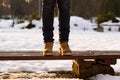 Female legs are standing on bench in winter sunny day. Blurred background of snow and sunset rays. Girk is walking in park. Royalty Free Stock Photo