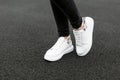 Female legs in stylish black jeans in white leather sneakers with snake pattern on the asphalt in the city. Young women on a walk