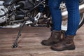 Female legs wearing brown leather safety boots for motorcycling are near motorbike, close up view Royalty Free Stock Photo