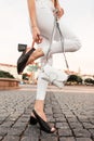 Female legs in white jeans in black leather sandals with a bag on a stone road in the city. Close-up Royalty Free Stock Photo