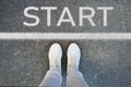 Female legs in white sneakers standing on the asphalt with the word start written on it