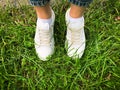 Female legs in whote leather sneakers standing on a grass in park, walking concept Royalty Free Stock Photo