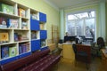 Female librarian sitting at the worktable in the library for primary school pupils, children books on shelves Royalty Free Stock Photo