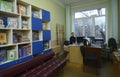 Female librarian sitting at the worktable in the library for primary school pupils, children books on shelves Royalty Free Stock Photo