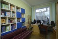 Female librarian sitting at the worktable in the library for primary school pupils, children books on shelves Royalty Free Stock Photo