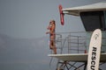 A female lifeguard at Ventura Harbor stands watch from a lifeguard tower at a breakwater