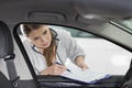 Female maintenance engineer with clipboard examining car's interior in workshop