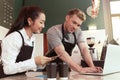 Female and male barista talking order on mobile phone and laptop computer while standing behind coffee shop counter bar, waitress Royalty Free Stock Photo