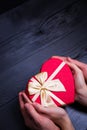 Female and male caucasian hands holding gift box in shape of heart on black wooden background Royalty Free Stock Photo