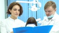 Female and male dentists holding a folder of documents discussing treatment in front of the patient in dental chair