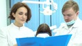 Female and male dentists holding a folder of documents discussing treatment in front of the patient in dental chair