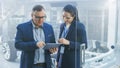 Female and Male Engineer Work in a High Tech Development Facility Holding a Tablet Computer. They Royalty Free Stock Photo