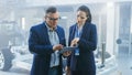 Female and Male Engineer Work in a High Tech Development Facility Holding a Tablet Computer. They Royalty Free Stock Photo