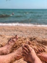 Female and male feet on a seashell sandy beach close-up against a background of azure sea water. Royalty Free Stock Photo