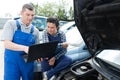 Female and male mechanic using laptop for examining car engine