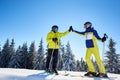 Female and male skiers high five to each other under sunny blue sky. Successful skiing up to mountain top. Full-length.