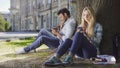 Female, male strangers sitting under tree, using cellphone, girl looking worried Royalty Free Stock Photo