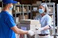 Female manager giving parcels boxes to courier wearing face masks in warehouse.