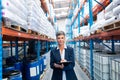 Female manager looking at camera while writing on clipboard in warehouse Royalty Free Stock Photo