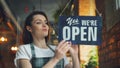 Female manager opening coffee shop in morning hanging open doorplate smiling