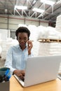 Female manager talking on headset while using laptop at desk in warehouse Royalty Free Stock Photo