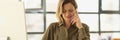 Female manager is talking on phone and taking notes in notebook while sitting at her desk in office. Royalty Free Stock Photo