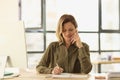 Female manager is talking on phone and taking notes in notebook while sitting at her desk in office. Royalty Free Stock Photo