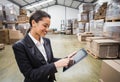African American woman in business attire tapping tablet and checking boxes on pallets in warehouse Royalty Free Stock Photo