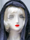 Female mannequin portrait with a white face, blond hair, long eyelashes, red lips and a black hood Royalty Free Stock Photo