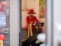 Female mannequin in a red outfit sits at table near the entrance to a small street cafe. Bright dress and straw hat attract Royalty Free Stock Photo