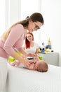 Female massage therapist or a doctor examining newborn baby boy with the mother watching in the background. Baby massage concept. Royalty Free Stock Photo