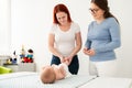 Female massage therapist teaching young mother how to massage her newborn baby boy. Baby massage concept.