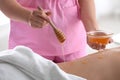 Female masseur using honey for spa procedure in salon