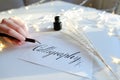 Female master of lettering of ink writes word on paper, sitting Royalty Free Stock Photo