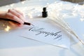 Female master of lettering of ink writes word on paper, sitting Royalty Free Stock Photo